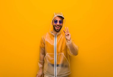 Üç numarayı gösteren yağmurluk giyen genç bir adam.