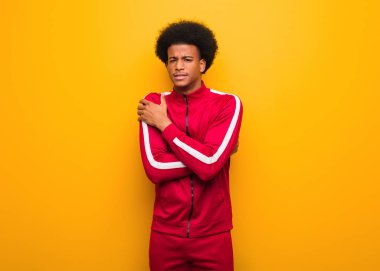 Turuncu bir duvarın üzerinden geçen genç bir zenci düşük sıcaklıktan dolayı soğuyor.