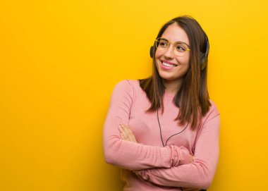 Genç, sevimli bir kadın müzik dinliyor, kendine güvenen, kollarını kavuşturup, yukarı bakıyor.