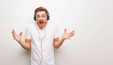 Genç kızıl saçlı adam zaferi ya da başarıyı kutluyor. Kulaklıkla müzik dinlemek..