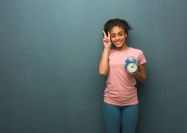 Young black woman fun and happy doing a gesture of victory. She is holding an alarm clock.