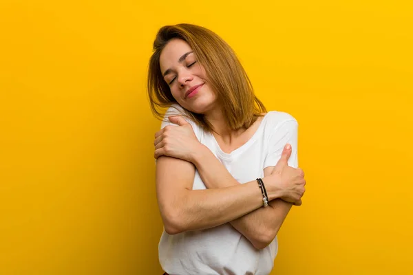 Young natural caucasian woman hugs herself, smiling carefree and happy.