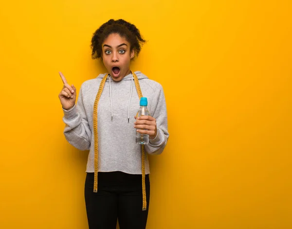 Young fitness black woman pointing to the side.Holding a water bottle.