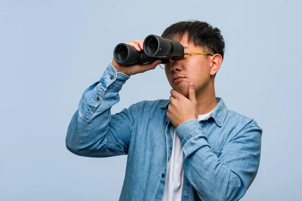 Young Chinese Man Holding Binoculars Doubting Confused — Stock Photo, Image