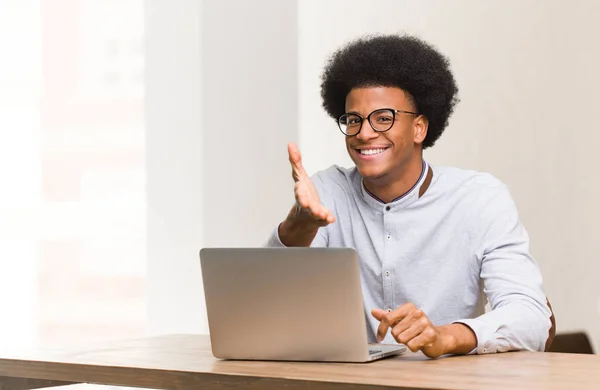 Young black man using his laptop reaching out to greet someone