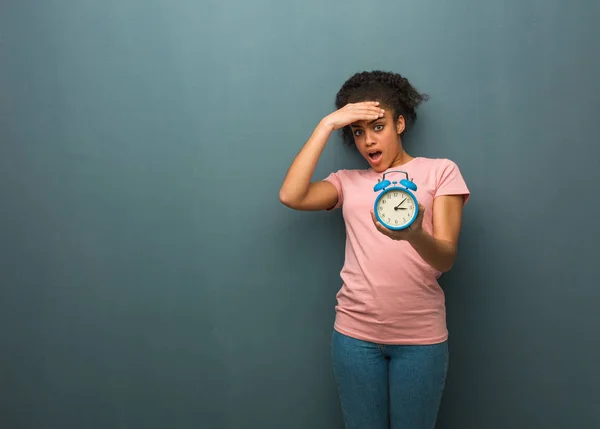 Young black woman forgetful, realize something. She is holding an alarm clock.