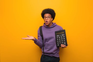 Genç Afrikalı Amerikalı öğrenci elinde bir hesap makinesi, elinde bir şey tutuyor.