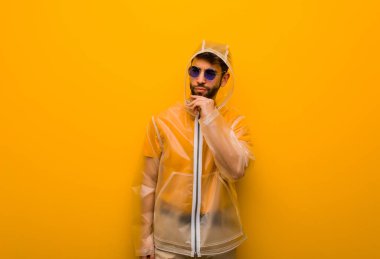 Yağmurluk giyen genç adam şüpheleniyor ve kafası karışık.