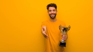 Elinde bir kupa tutan genç adam birine selam veriyor.