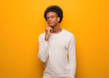 Turuncu bir duvar üzerinde genç Afrikalı Amerikalı adam şüphe ve karıştı