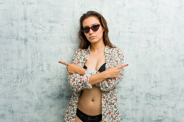 Young European Woman Wearing Bikini Points Sideways Trying Choose Two — 스톡 사진