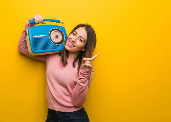 Young cute woman holding a vintage radio pointing to the side with finger