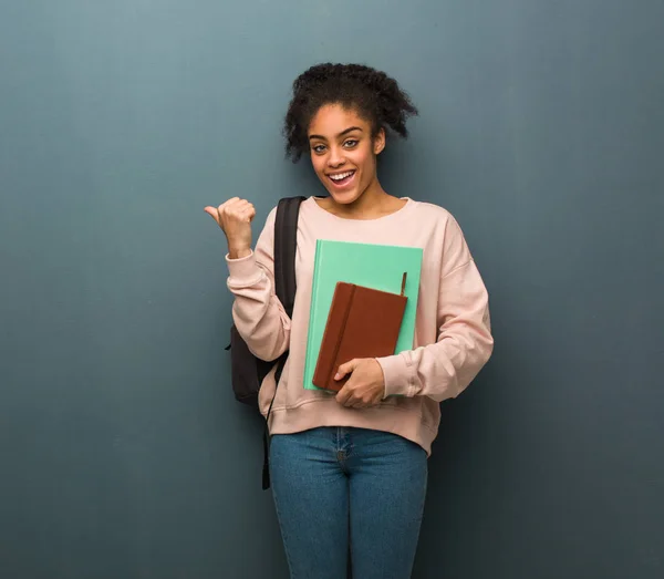 Young student black woman smiling and pointing to the side. She is holding books.