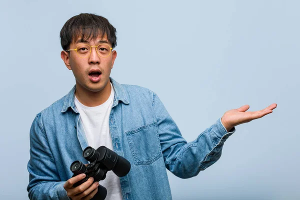 Young chinese man holding a binoculars holding something on palm hand