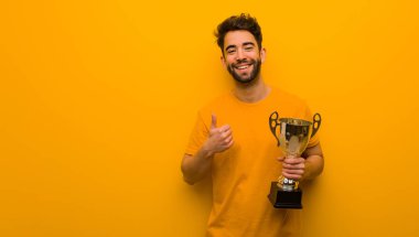 Elinde bir kupa tutan genç adam gülümsüyor ve başparmağını kaldırıyor.