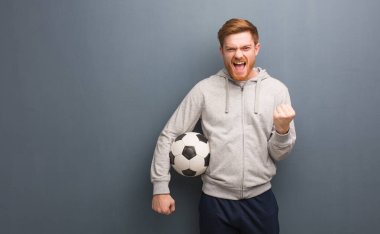 Genç kızıl saçlı fitness adamı şaşırdı ve şok oldu. Elinde bir futbol topu tutuyor..