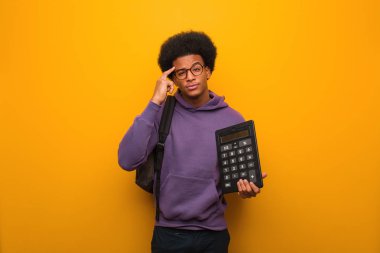 Genç Afrikalı Amerikalı öğrenci elinde hesap makinesiyle bir fikir düşünüyor.