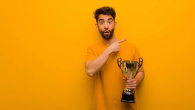 Elinde bir kupa tutan genç adam parmağıyla kenarı işaret ediyor.