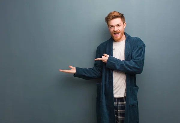 Young redhead man in pajama holding something with hand