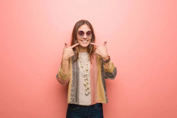 Young hippie woman on pink background smiles, pointing mouth