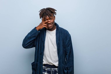 Genç Afrikalı siyah adam pijama giyip kameraya parmaklarıyla göz kırpıyor, yüzünü kapatmaktan utanıyor..