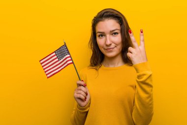 Amerika Birleşik Devletleri bayrağı taşıyan genç bir kadın iki numarayı parmaklarıyla gösteriyor..