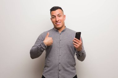 Elinde telefon tutan genç latin adam şaşırdı, başarılı ve başarılı hissediyor.