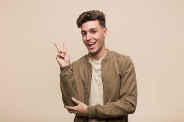 Kahverengi ceketli genç beyaz adam neşeli ve tasasız parmaklarıyla barış sembolü gösteriyor..