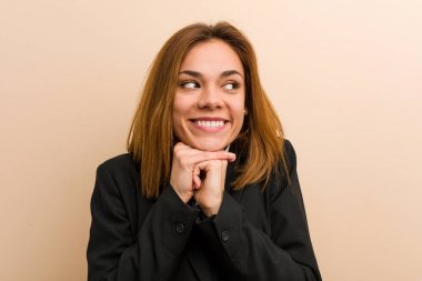 Genç beyaz iş kadını ellerini çenesinin altında tutuyor, mutlu bir şekilde yan tarafa bakıyor..