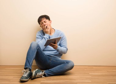 Genç Çinli adam tabletini kullanıyor yorgun ve çok uykulu.