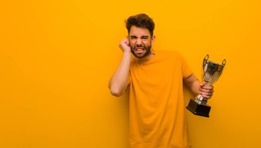 Elleriyle kulaklarını kapatan bir kupa tutan genç adam.