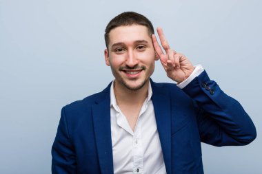 Genç beyaz adam zafer işareti gösteriyor ve gülümsüyor..
