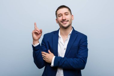 Genç beyaz adam işaret parmağıyla işaret ederek gülümsüyor..