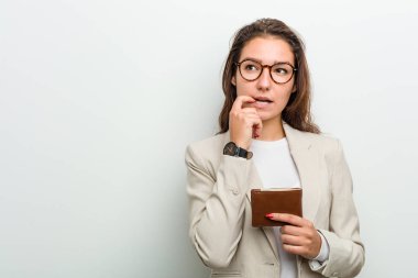 Genç Avrupalı iş kadını cüzdanını tutarken rahat bir şekilde fotokopi odasına bakıyor..