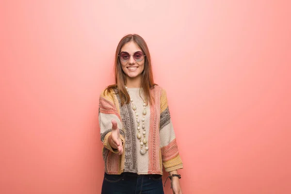 Young hippie woman on pink background reaching out to greet someone