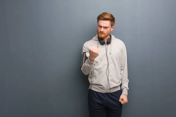 Young fitness redhead man showing fist to front, angry expression
