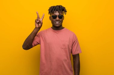 Gündelik siyah gözlüklü genç adam zafer işareti gösteriyor ve gülümsüyor..