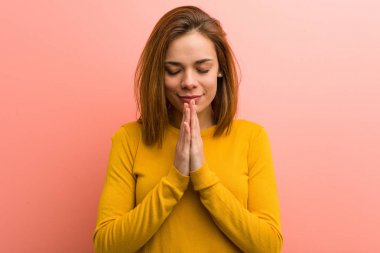 Young pretty young woman holding hands in pray near mouth, feels confident.
