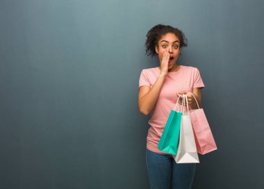 Genç siyahi kadın ön tarafa mutlu bir şey bağırıyor. Elinde bir alışveriş çantası var..