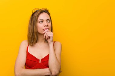 Bikini ve güneş gözlüğü takan beyaz bir kadın şüpheli ve şüpheci bir ifadeyle yana bakıyor..