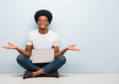 Genç siyahi bir adam dizüstü bilgisayarıyla yerde oturuyor.