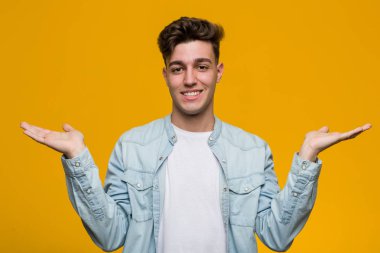 Kot gömlek giyen genç ve yakışıklı bir öğrenci kollarıyla terazi yapıyor, mutlu ve kendinden emin hissediyor..