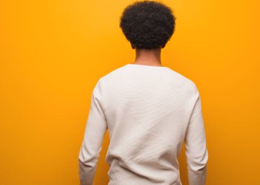 Genç Afro-Amerikan bir adam turuncu bir duvarın arkasında, geriye bakıyor.