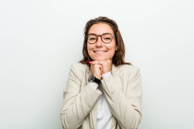 Genç Avrupalı iş kadını ellerini çenesinin altında tutuyor, mutlu bir şekilde yan tarafa bakıyor..