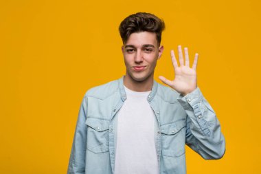 Kot gömlek giyen genç ve yakışıklı bir öğrenci gülümseyerek parmaklarıyla 5 numarayı gösteriyor..