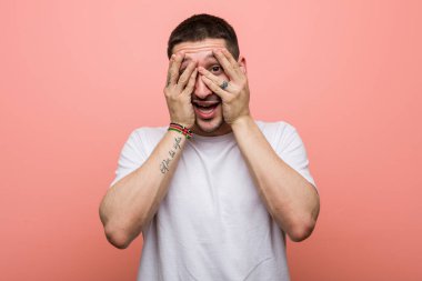 Genç sıradan bir adam parmaklarının arasından korkmuş ve gergin bir şekilde göz kırpıyor..