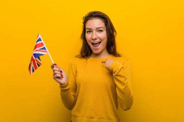 Birleşik krallık bayrağını tutan genç Avrupalı kadın kendini göstererek şaşırdı, geniş bir gülümseme içinde..