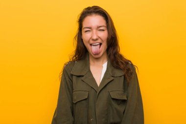 Genç Avrupalı kadın sarı arka plan üzerinde izole komik ve dostu dil dışarı yapışması.