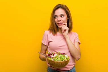 Young healthy woman holding a salad relaxed thinking about something looking at a copy space.