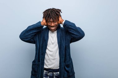 Genç Afrikalı siyah adam pijama giyip kulaklarını elleriyle kapatıyor ve çok ses duymamaya çalışıyor..